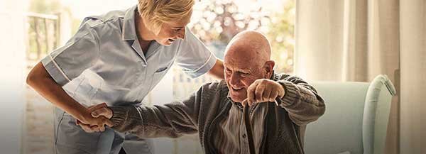 Sköterska hjälper en gammal man att ställa sig upp - Äldreomsorg | © Getty Images